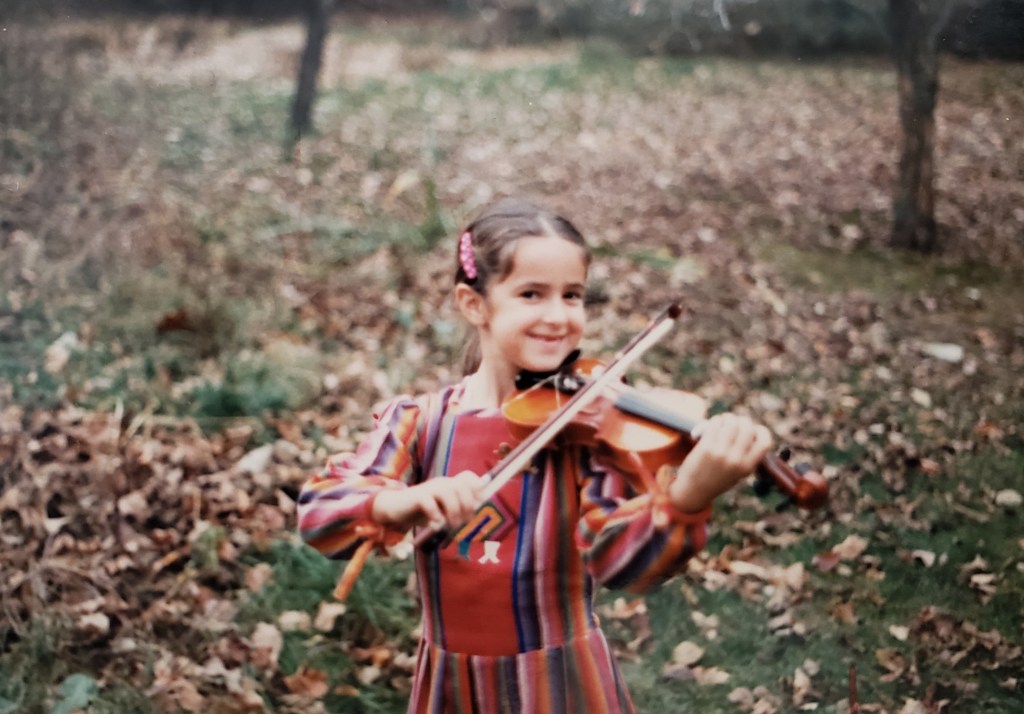 A child plays violin outside in the fall