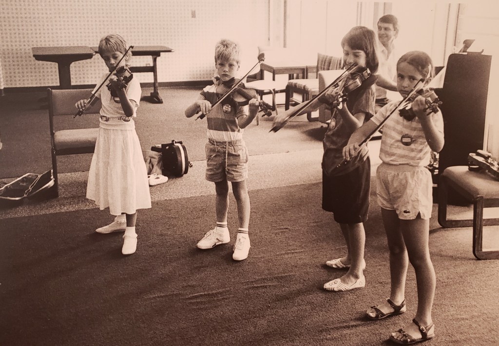 A group of children play violin together